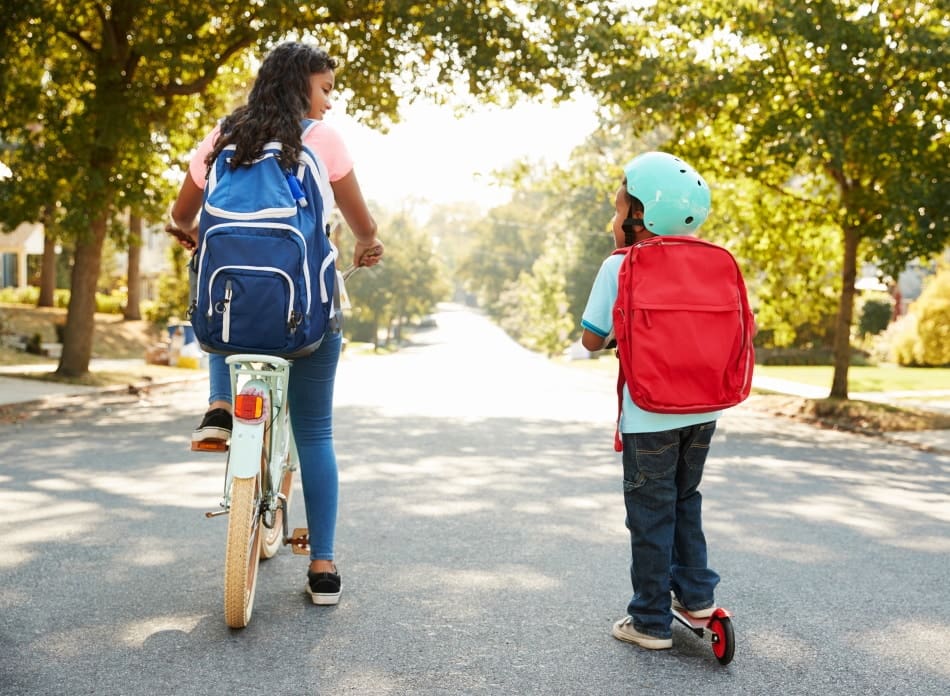 Sister With Brother Riding Scooter And Bike To School