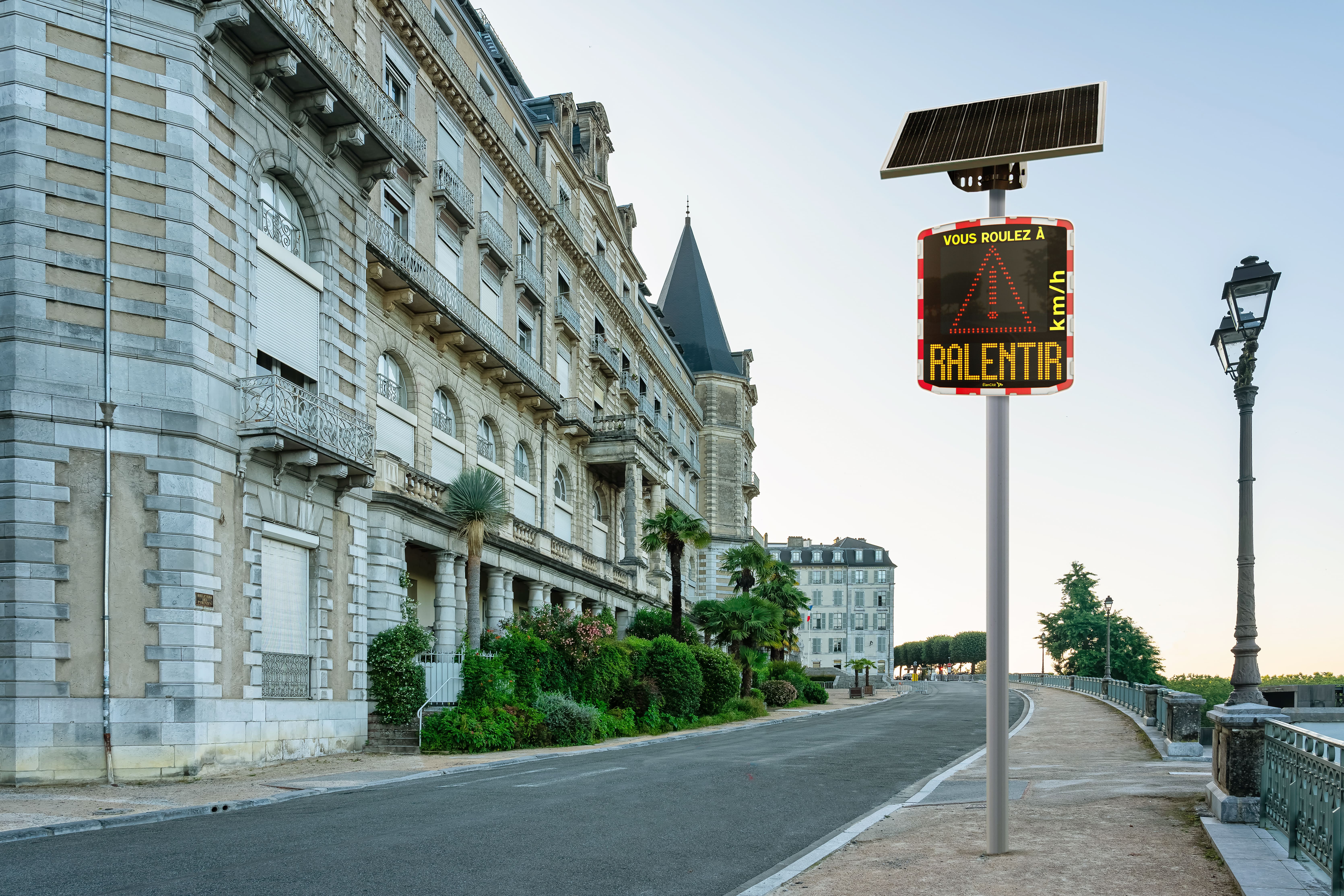 Un radar pédagogique solaire instalé aux abords d'une rue piétonne qui affiche un triangle et un message de prévention "RALENTIR"